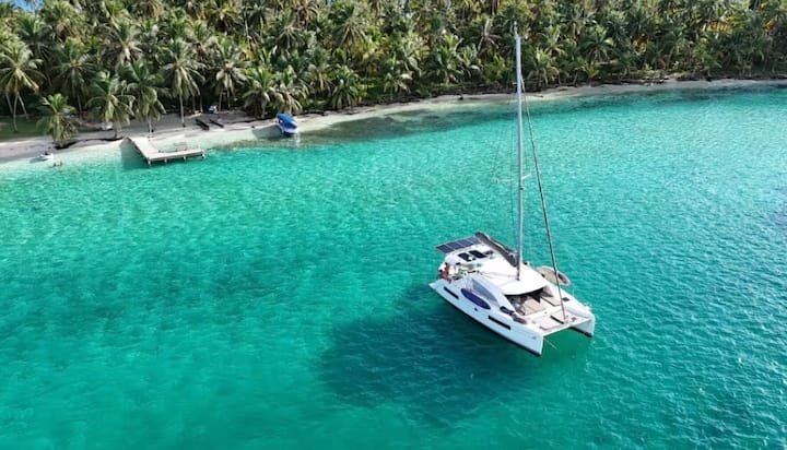 Aerial view of the Brittany Wind Leopard 40 catamaran anchored in turquoise water beside a palm-lined San Blas island